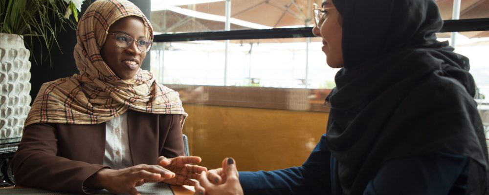 Muslim female colleagues chatting during lunch break. Business women in hijabs sitting in coffee shop and discussing project. Business lunch break concept